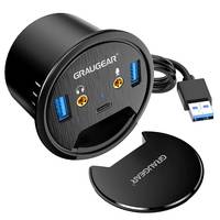 Schwarze GRAUGEAR Desktop-Kabelführung mit zwei USB-A-Anschlüssen, Kopfhörer- und Mikrofonbuchsen, USB-C-Anschluss und angeschlossenem USB-Kabel; Schutzkappe separat abgebildet.