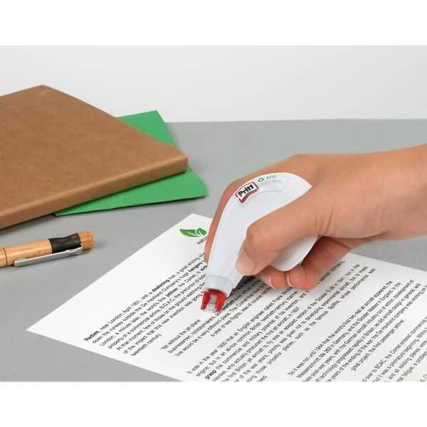 Hand benutzt einen weißen Korrekturband-Spender, um Text auf einem gedruckten Dokument abzudecken, daneben liegen ein Notizbuch und ein Bleistift.
