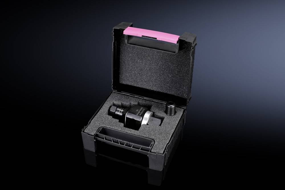 Ein schwarzer Kunststoffkoffer mit einem rosa Griff enthält ein schwarzes Gerät mit Metallkomponenten und einer kleinen, separaten schwarzen Kappe, die in Schaumstoffpolsterung eingebettet sind.