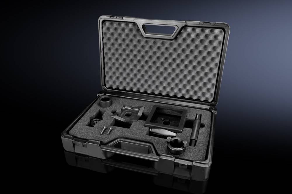 Schwarze Schutzbox mit Schaumstoffeinsatz geöffnet, die verschiedene metallische mechanische Bauteile enthält und auf einer dunklen Oberfläche ruht.