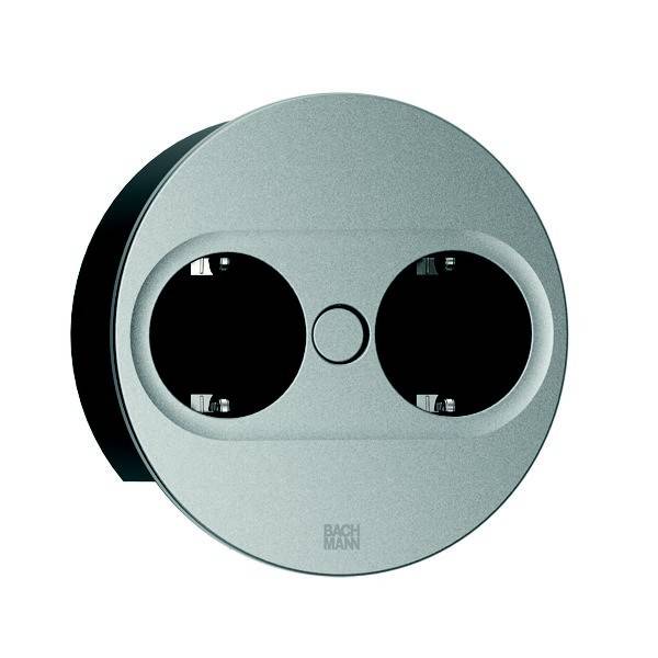 Eine kreisförmige metallische Steckdose mit zwei Anschlüssen, für moderne Inneneinrichtungen konzipiert, am unteren Rand mit 'Bachman' beschriftet.