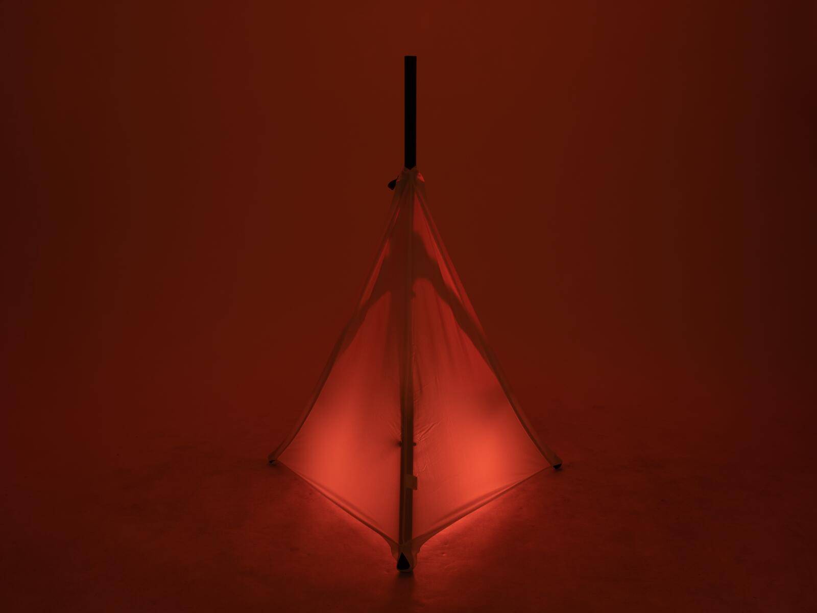 Eine geschlossene Regenschirm steht aufrecht, von rotem Licht beleuchtet, und erzeugt einen Schattenbildeffekt vor einem dunklen Hintergrund.