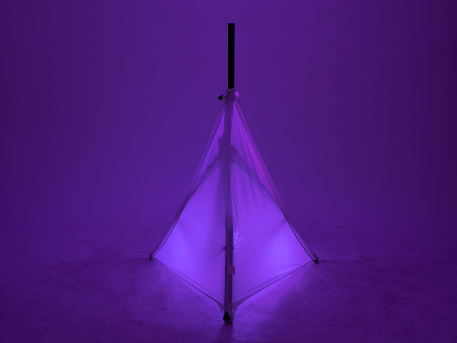 Ein Regenschirm wird von violettem Licht von unten beleuchtet und wirft einen symmetrischen Schatten auf die umgebende Oberfläche.