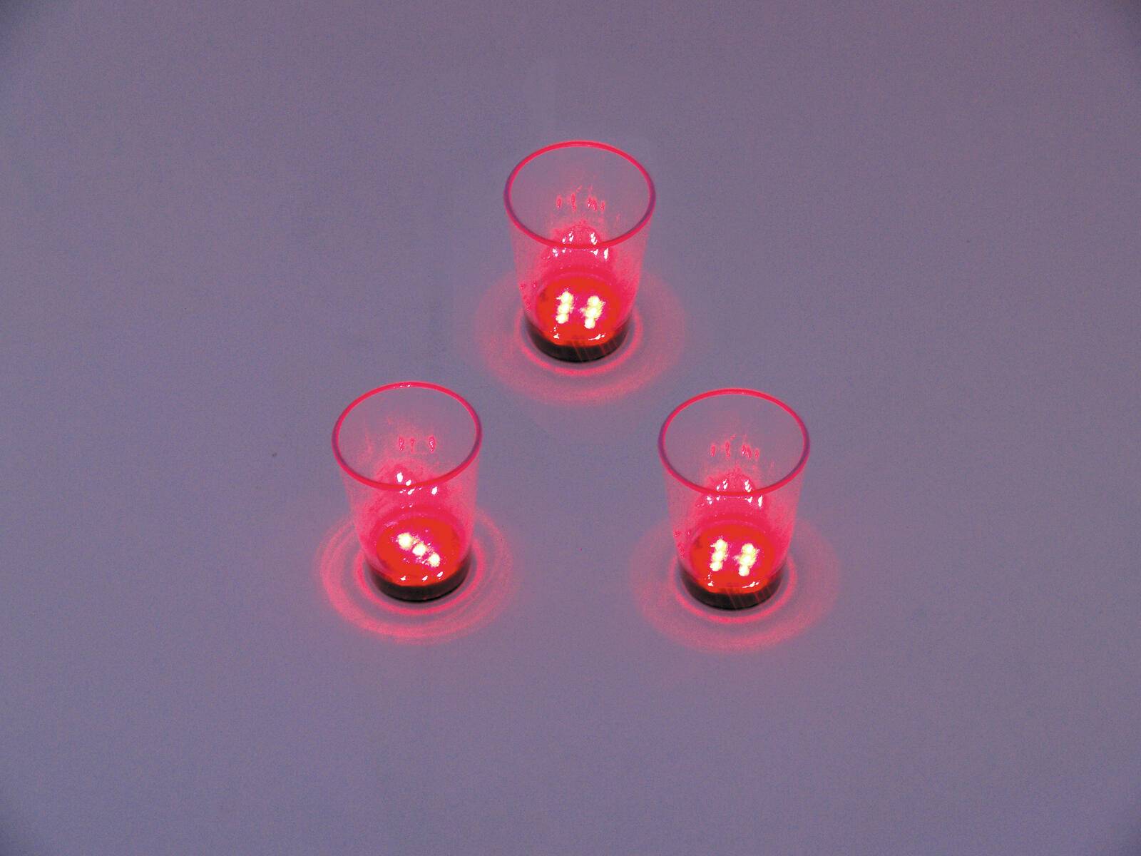 Drei kleine rote LED-Lichter in durchsichtigen Bechern, in einem Dreieck auf einer reflektierenden Oberfläche angeordnet, die kreisförmige rote Glühen werfen.
