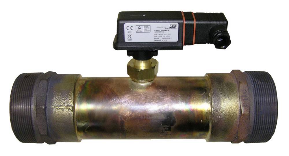 Ein metallischer Wasserdurchflusssensor mit einer zentralen Leitung und angeschlossenem digitalen Messgerät zur Anzeige der Messwerte.