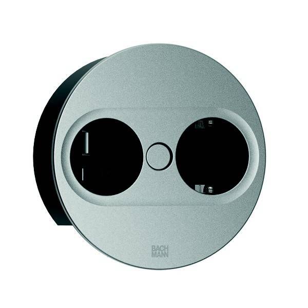 Eine runde, metallische Steckdose mit zwei Steckplätzen und einem zentralen Knopf, von Bachmann entworfen, geeignet für moderne Inneneinrichtungen.