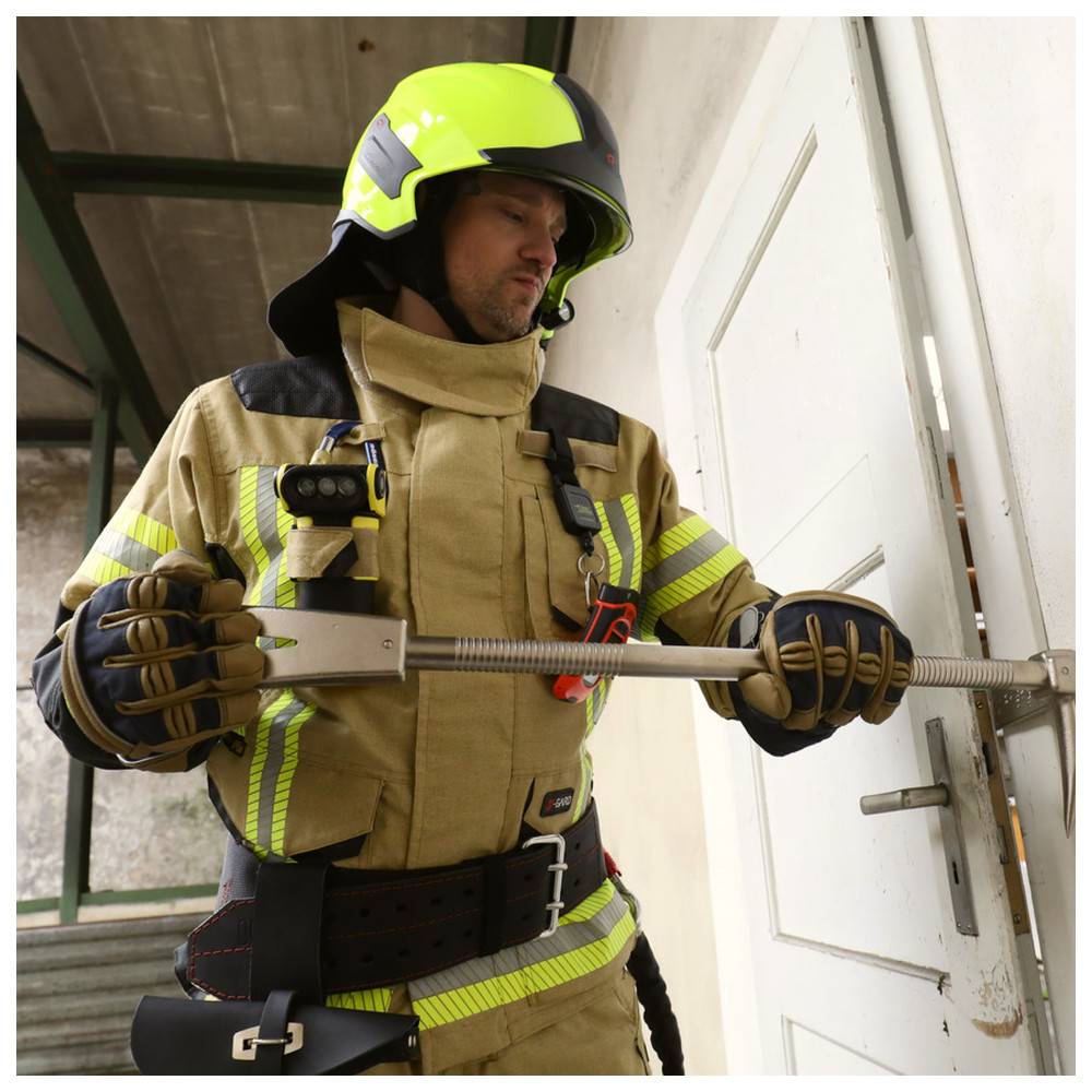 Ein Feuerwehrmann mit gelbem Helm und Uniform verwendet eine Halligan-Brechstange, um eine weiße Tür in einer Notsituation zu öffnen.