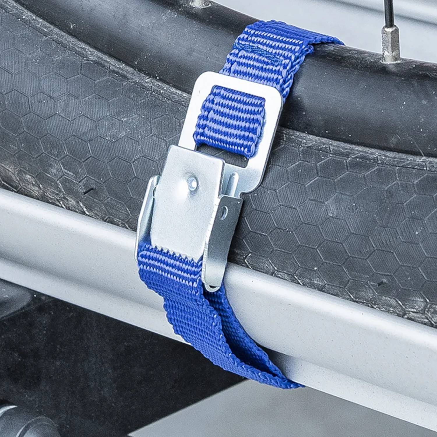 Ein Nahaufnahmebild eines blauen Riemens, der einen Fahrradreifen an einem Dachträger sichert. Der Riemen ist mit einer Metallschnalle festgezogen.