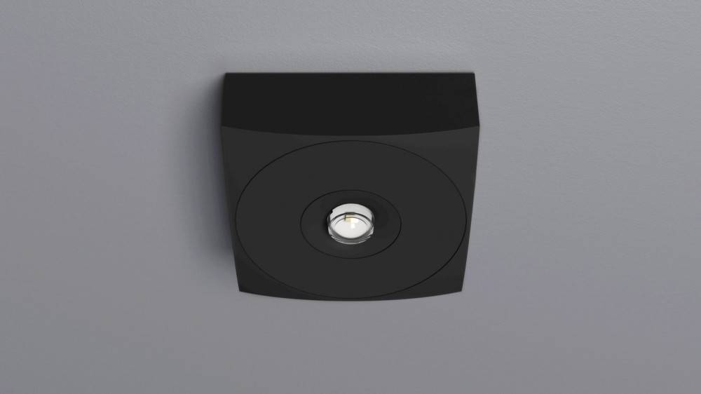 Eine schwarze, quadratische Deckeneinbauleuchte mit vertieftem Design, ausgestattet mit einer zentralen LED-Lampe, an einer grauen Decke montiert.