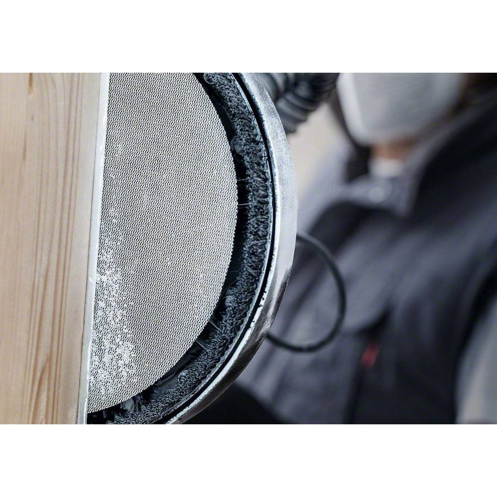 Eine Person, die ein Schleifwerkzeug auf einer Holzoberfläche verwendet und eine Maske zum Schutz trägt. Das Schleifwerkzeug erzeugt feine Staubpartikel.