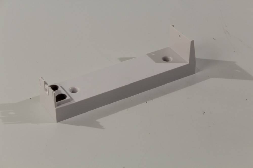 Ein weißer rechteckiger Halter mit zwei kreisrunden Löchern und abgewinkelten Enden, der auf einer glatten Oberfläche liegt und rechts einen leichten Schatten wirft.