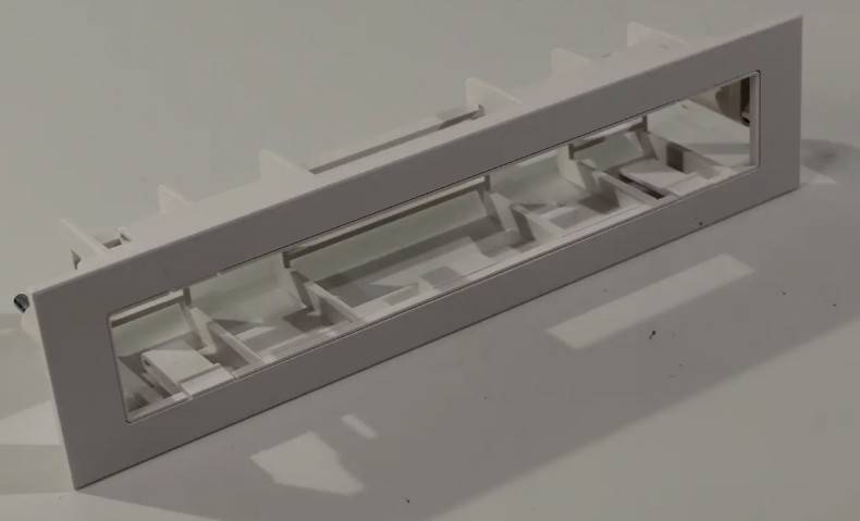 Eine Nahaufnahme eines weißen, rechteckigen Plastikbehälters mit Trennwänden im Inneren, der einen Schatten auf einer grauen Oberfläche wirft.