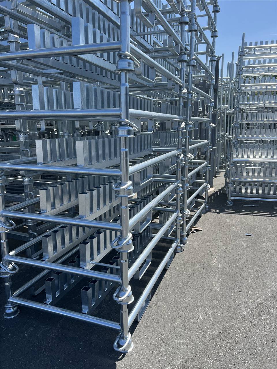 Metallgerüste, die in Reihen auf einer gepflasterten Oberfläche unter hellem Sonnenlicht gestapelt sind, was auf eine industrielle oder Baustelle hindeutet.