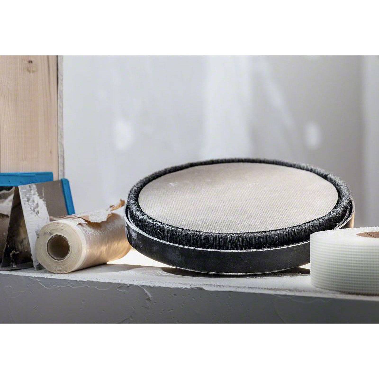 Ein Gipspaneel-Schleifwerkzeug steht auf einem Regal, umgeben von einer Rolle Klebeband, einer Kelle und einer Rolle Schleifpapier, einsatzbereit.