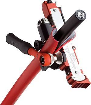 Eine rote Fahrradbremse mit einem Metallhebel und schwarzem Griff wird in Nahaufnahme gezeigt, ausgestattet mit einer Einstellschraube zur Spannungsregulierung.