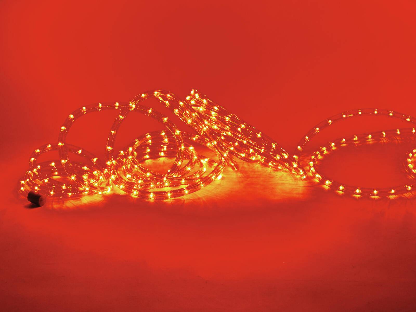 Eine aufgewickelte Schnur aus leuchtend orangefarbenen Lichterketten vor einem lebendigen roten Hintergrund, die eine warme und festliche Atmosphäre schafft.