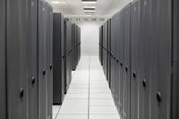 Ein schmaler Serverraum-Flur mit hohen schwarzen Datenschränken auf beiden Seiten, fotografiert aus der Mitte eines Korridors mit weißen Fliesen.