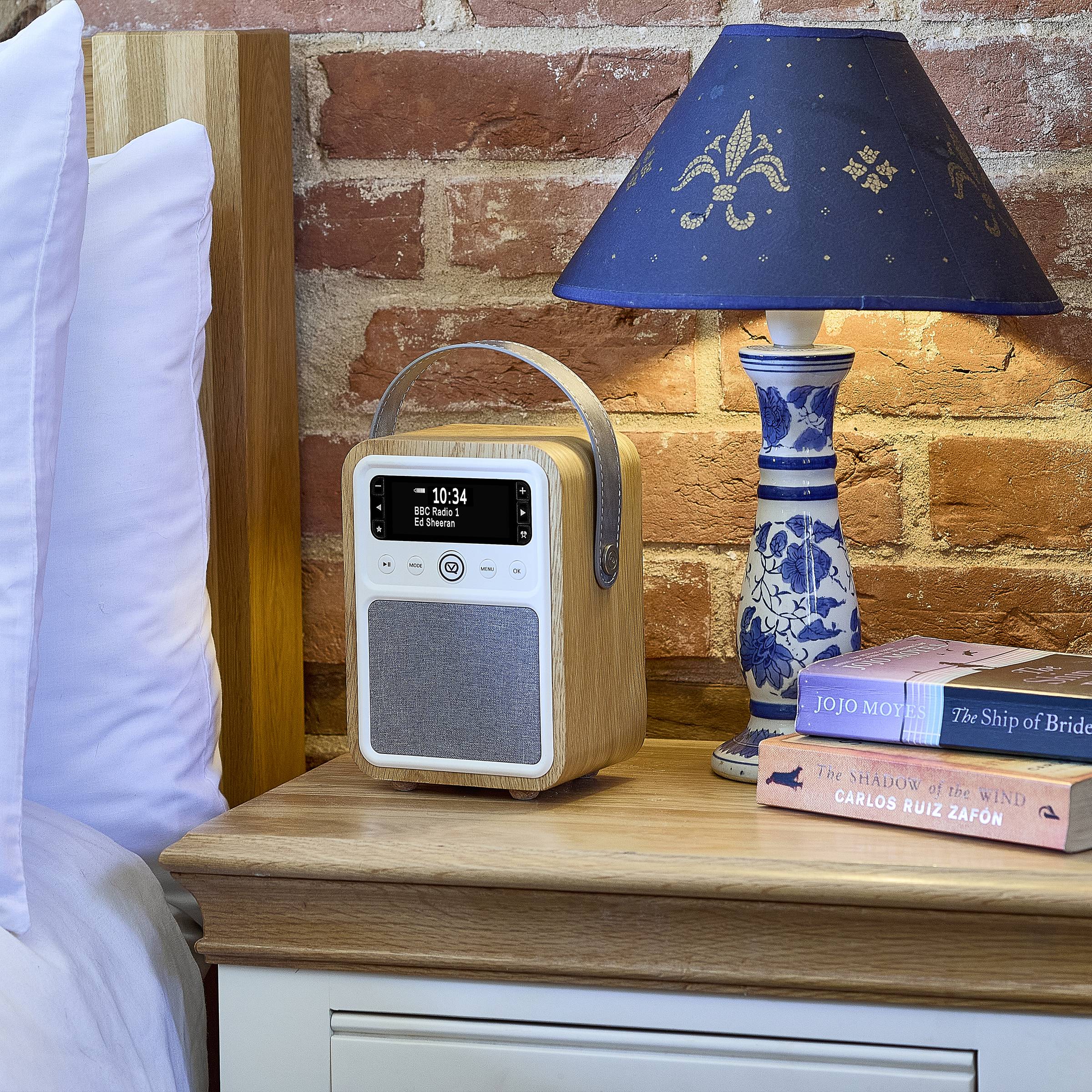 Ein Nachttisch mit einem digitalen Radio, einer blauen Lampe und Büchern mit den Titeln „Der Schatten des Windes