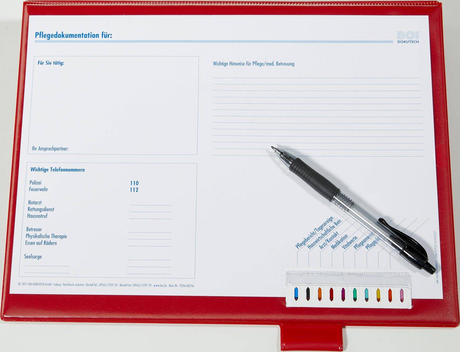 Ein roter Ordner auf einer weißen Oberfläche mit einem Stift darin. Der Ordner hat Textfelder für Dokumentation und Notizen sowie einen Abschnitt für Telefonnummern mit der Bezeichnung 