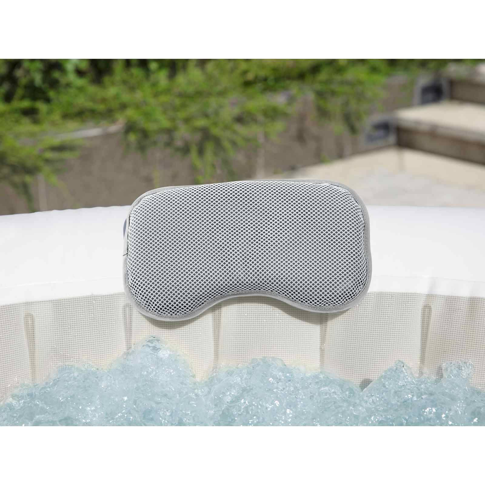Graues Netzstoffnackenkissen, das am Rand eines weißen Whirlpools ruht, mit sprudelndem Wasser darunter und verschwommenem Außenhintergrund.