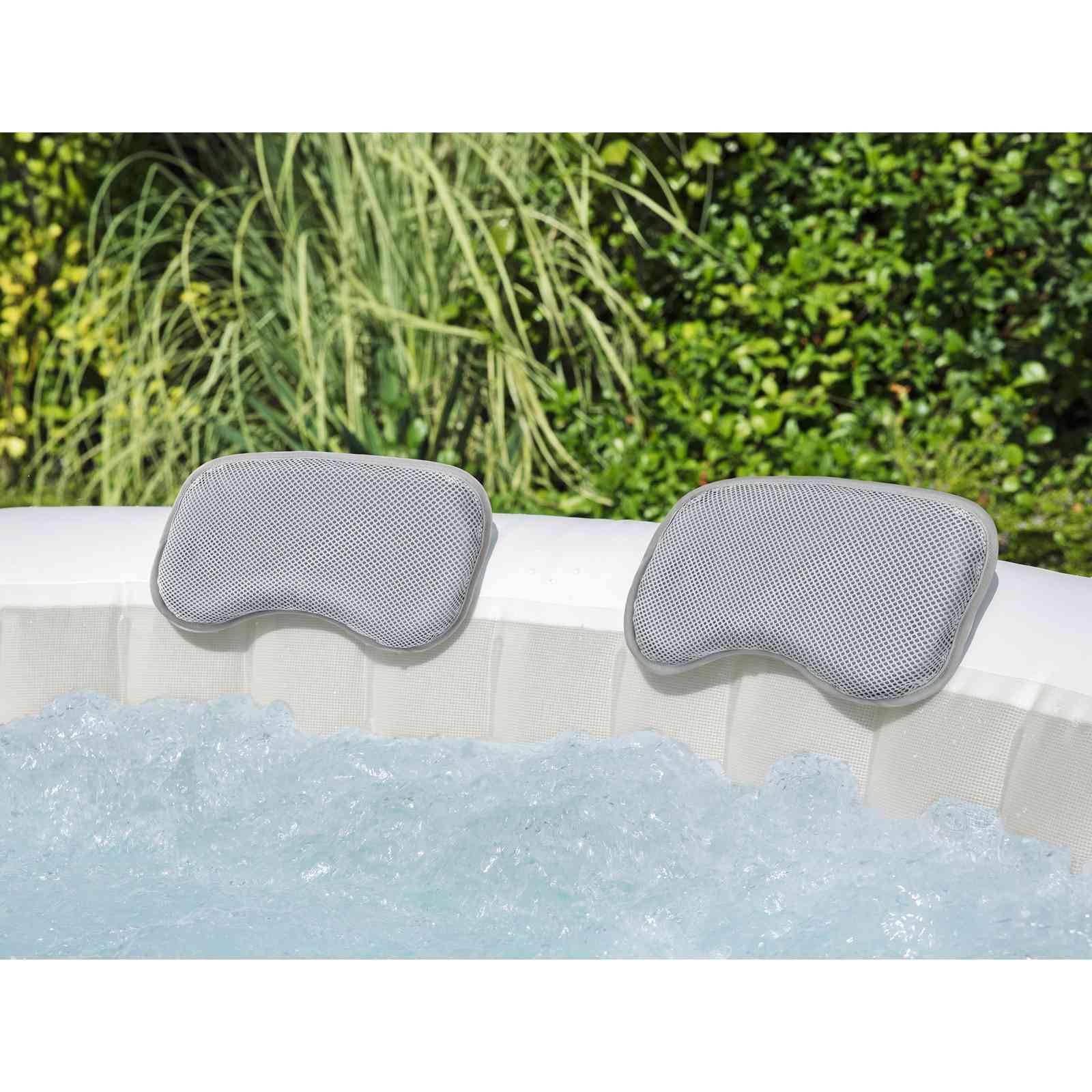 Zwei graue gepolsterte Kopfstützen am Rand eines sprudelnden Außen-Whirlpools mit grünem Laub im Hintergrund.