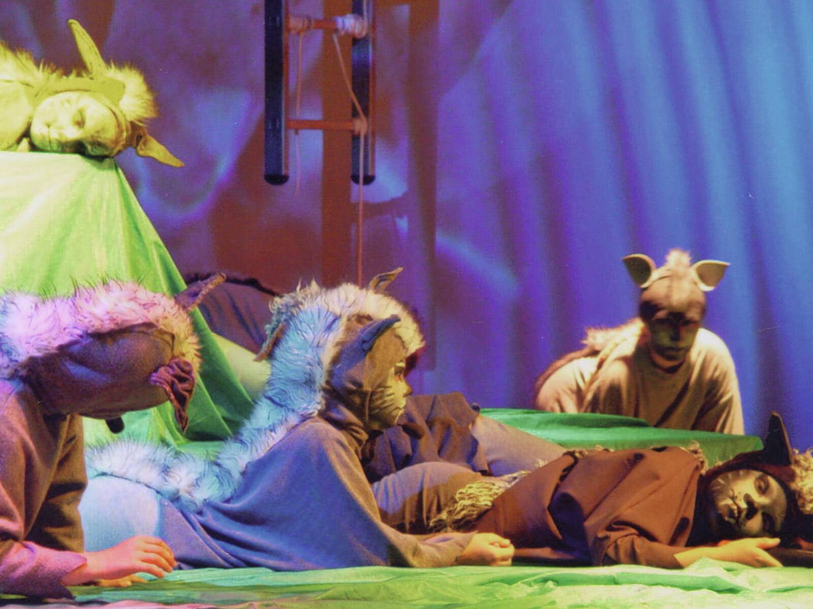 Schauspieler in Tierkostümen treten auf der Bühne auf. Die Szene ist farbenfroh und dramatisch, mit ausdrucksstarker Körpersprache und dynamischer Beleuchtung.