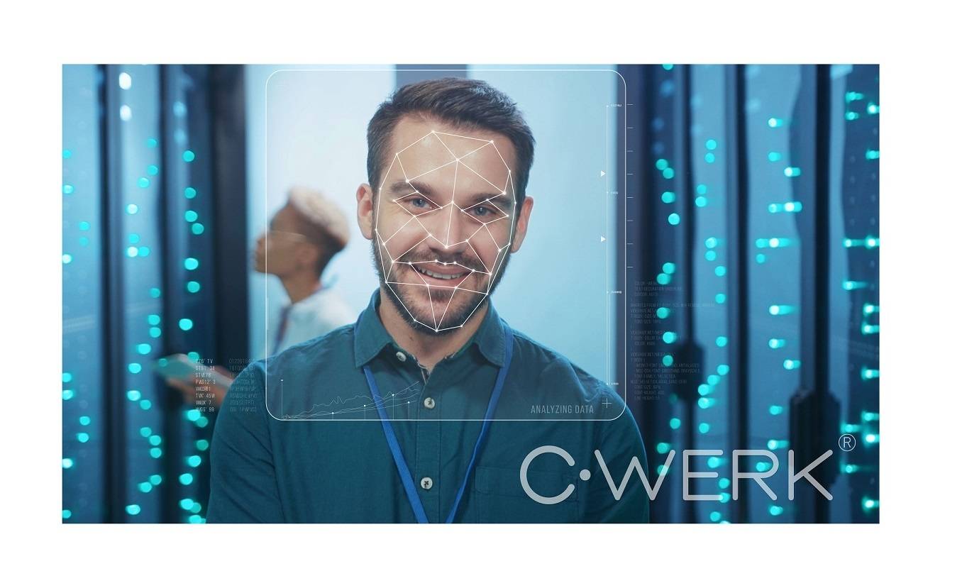 Ein Mann steht lächelnd in einem Serverraum, mit einer Gesichtserkennung-Überlagerung, die Daten analysiert. Blaue Lichter leuchten sanft im Hintergrund.