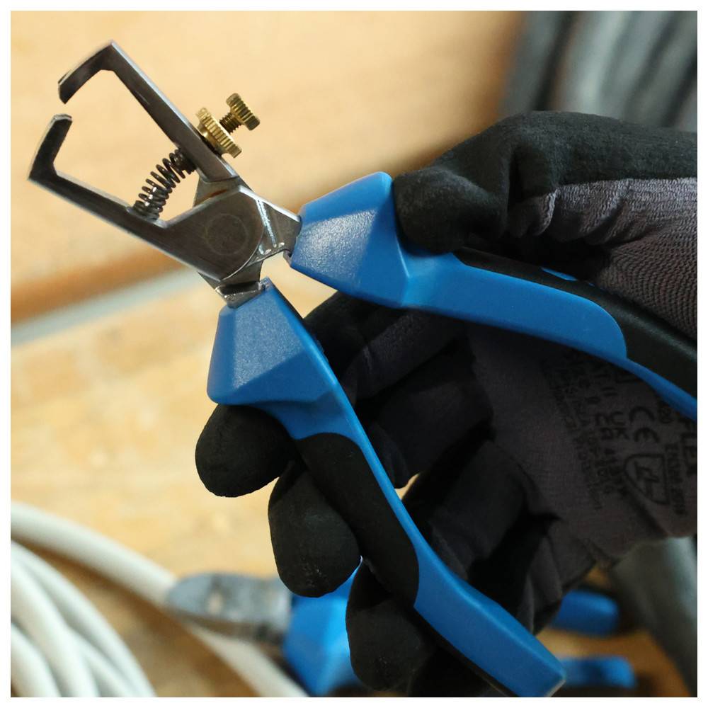 Eine Person mit Handschuhen hält ein blaues und silbernes Abisolierwerkzeug mit einer verstellbaren Messingschraube und bereitet sich darauf vor, ein weißes Kabel zu entfernen.