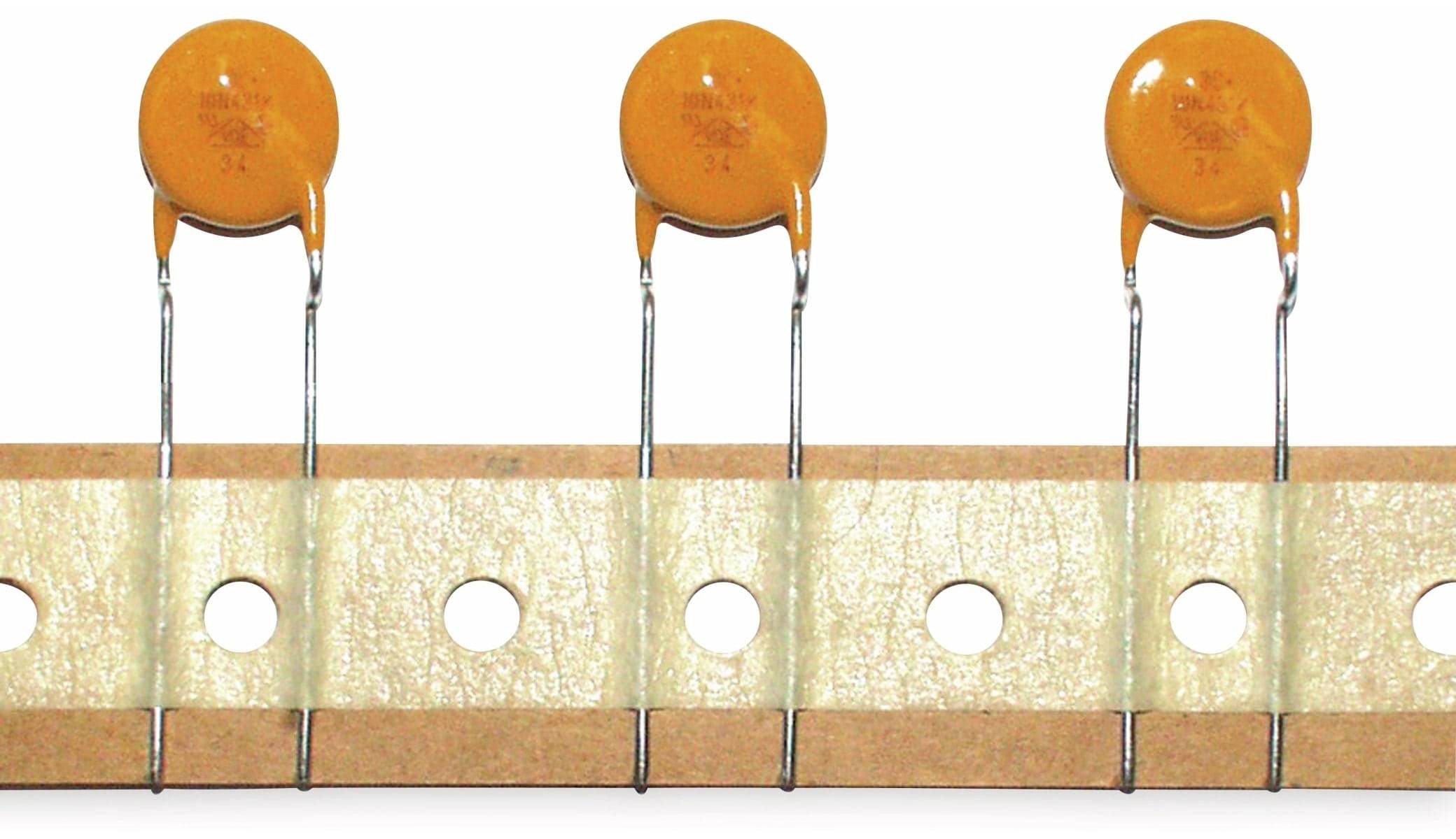 Das Bild zeigt eine Reihe von gelben keramischen Scheibenkondensatoren, die auf einem Streifen mit Löchern montiert sind. Sie werden in elektronischen Schaltungen zur Filterung verwendet.