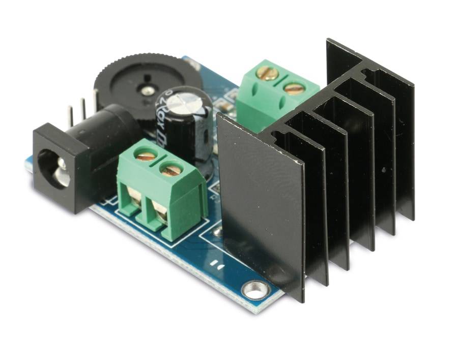 Eine blaue Platine mit einem schwarzen Kühlkörper, Kondensatoren und Anschlussklemmen, die für elektronische Komponenten und Projekte verwendet wird.