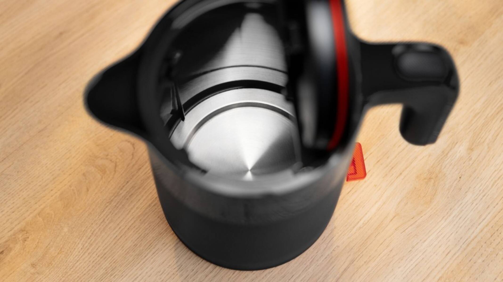 Innenansicht eines leeren Metallwasserkessels mit offenem Deckel, der auf einer Holzoberfläche steht. Das innere Heizelement ist sichtbar.