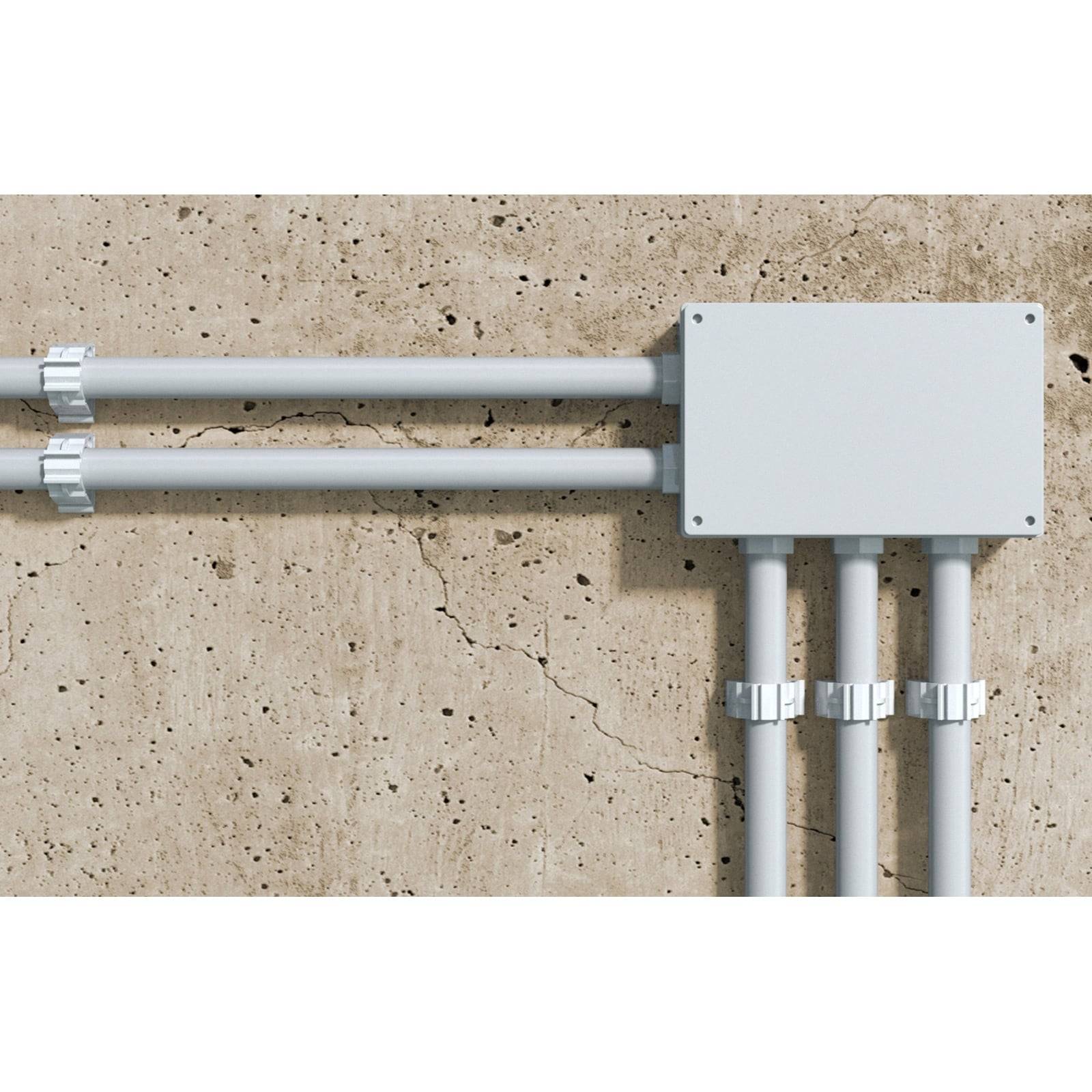 Eine weiße elektrische Verteilerdose, die an einer strukturierten Betonwand montiert ist, mit mehreren Leitungsrohren, die an beiden Seiten angeschlossen sind.