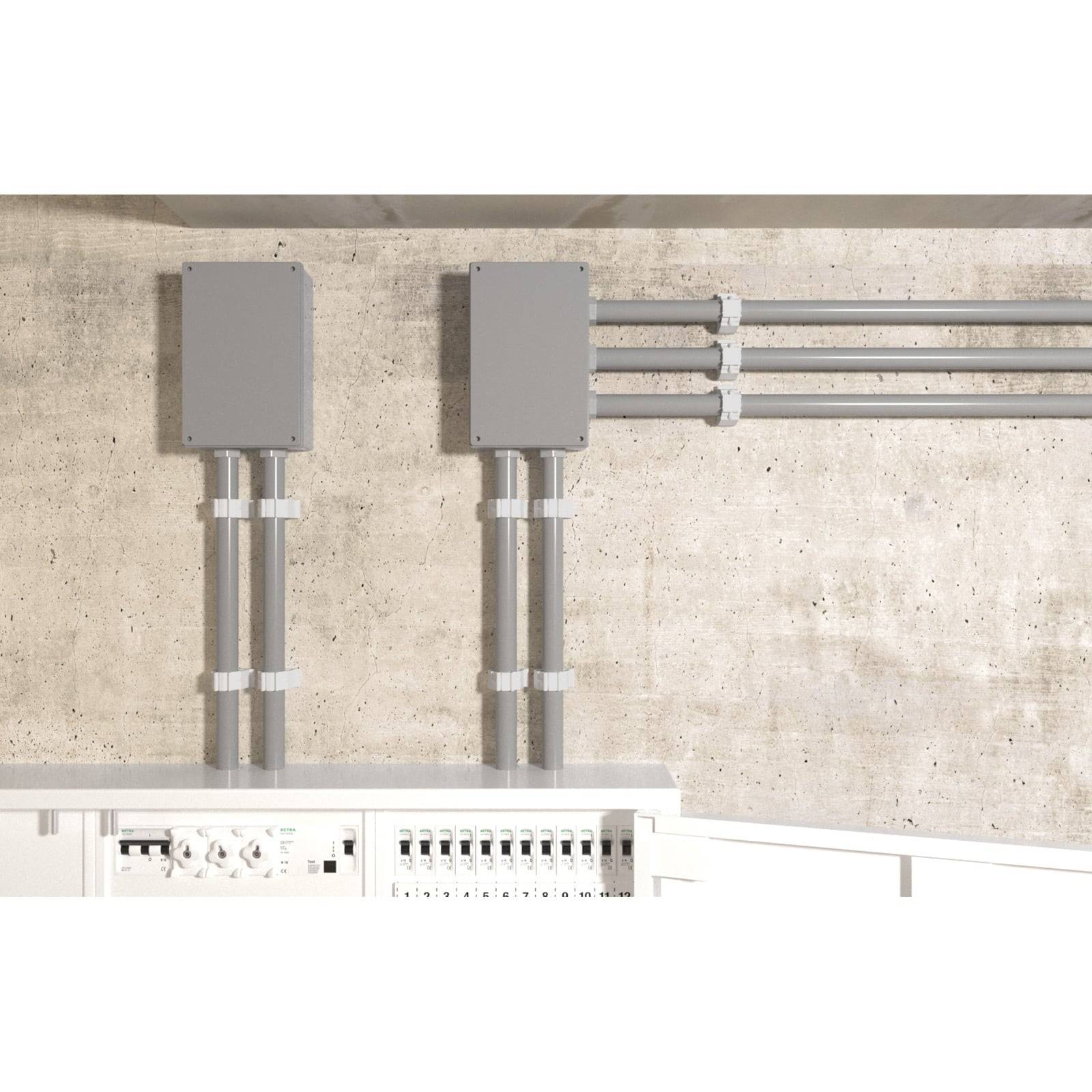 Elektrische Verteilertafel mit Metallkonduit und grauen Kästen, die an einer Betonwand montiert ist und eine saubere und organisierte Anordnung zeigt.