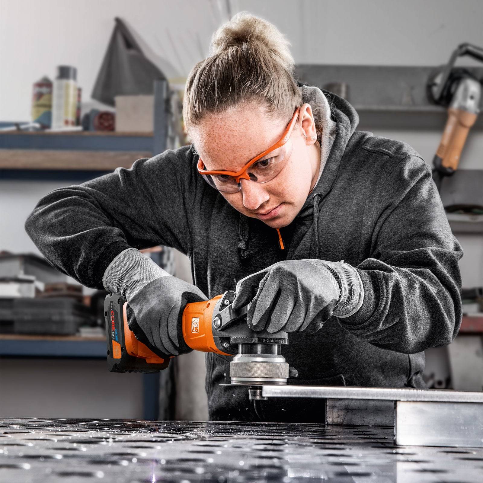 Eine Person mit Sicherheitsbrille und Handschuhen bedient ein Elektrowerkzeug, um eine Metalloberfläche in einer Werkstattumgebung zu schleifen.