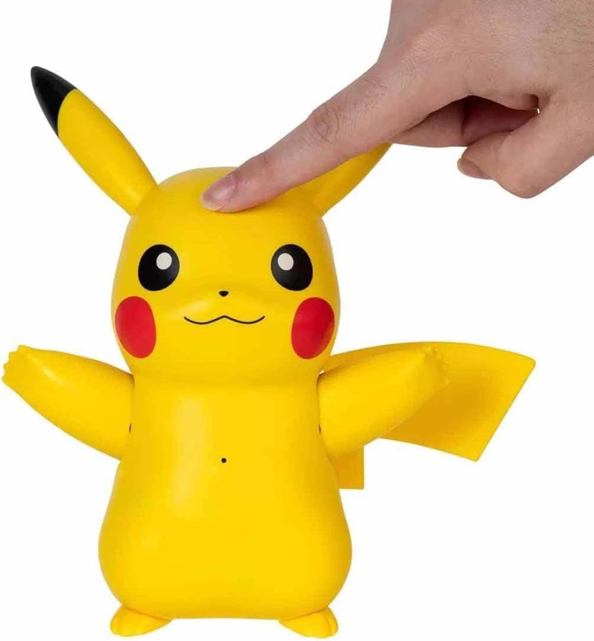 Eine gelbe Pikachu-Spielzeugfigur mit roten Wangen wird mit einem Finger auf ihrem Kopf berührt, was auf Interaktion oder Aktivierung hindeutet.