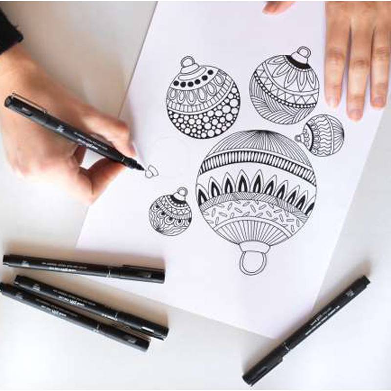 Eine Person zeichnet komplizierte Muster auf Weihnachtsschmuck auf Papier, umgeben von schwarzen Markern.