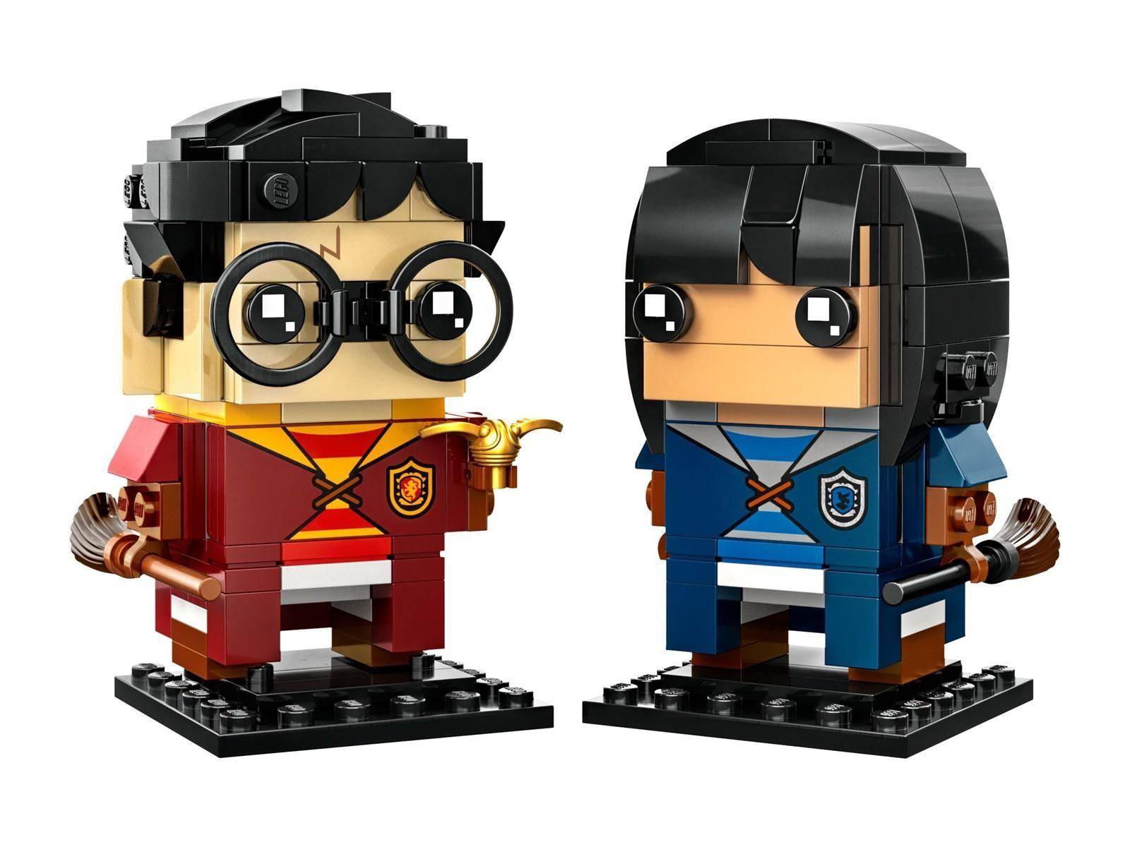 Zwei LEGO-ähnliche Minifiguren-Statuen auf schwarzen Sockeln, eine in einem roten Gewand mit Brille und Zauberstab, eine in einem blauen Gewand mit einem Zauberstab.