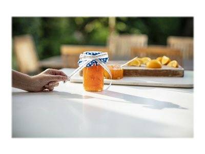 Eine Hand greift nach einem Glas mit orangefarbener Marmelade auf einem Tisch, mit geschnittenen Orangen im Hintergrund.