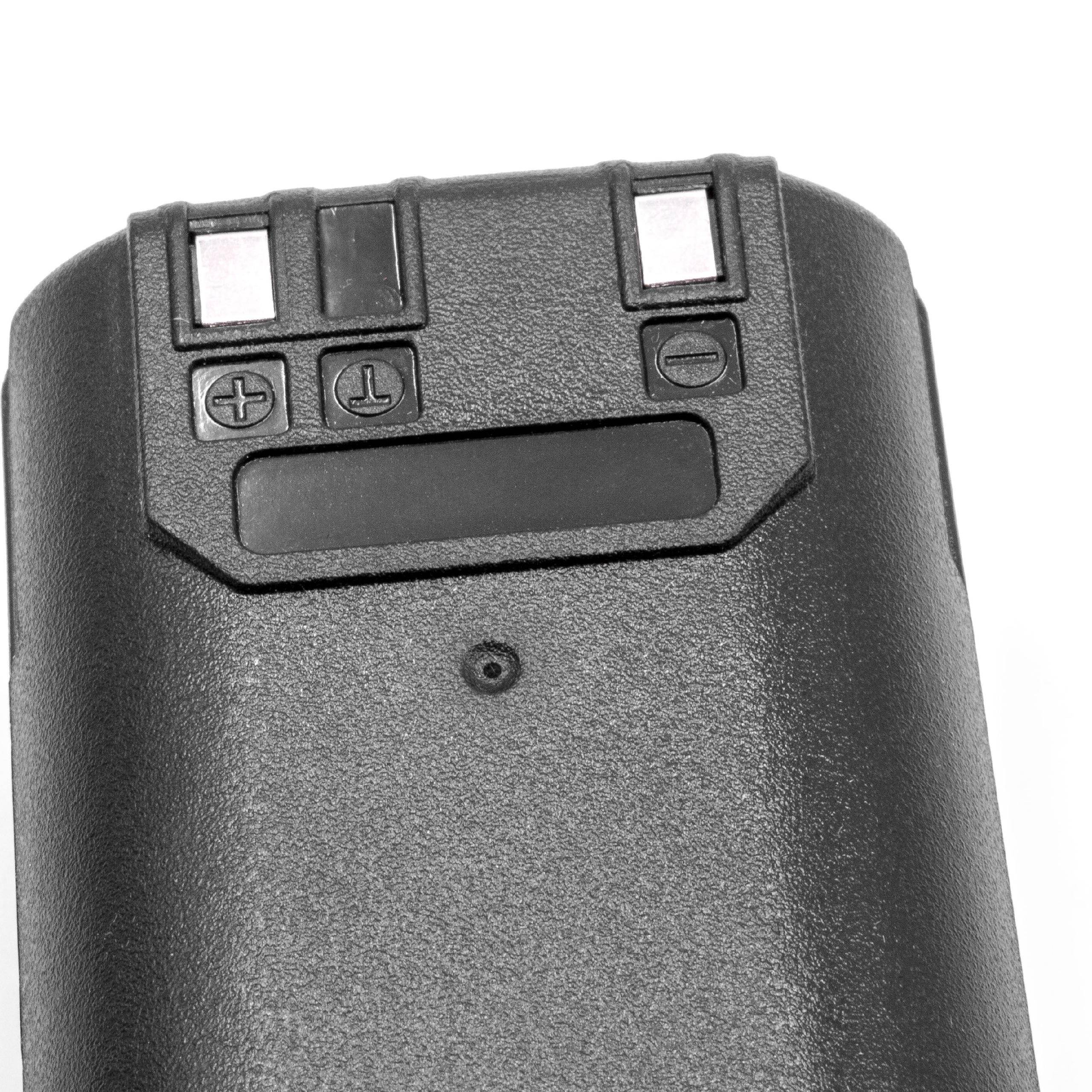 Eine schwarze Kunststoffkamerabatterie mit Plus- und Minuszeichen, einer Auslösetaste und zwei Metallkontakten, von oben betrachtet.