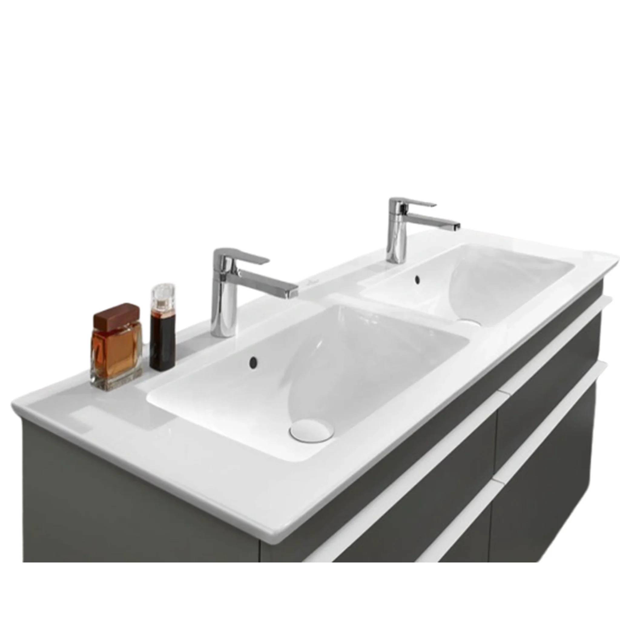 Doppelwaschtisch mit zwei Chromarmaturen und Toilettenartikeln auf der linken Seite.