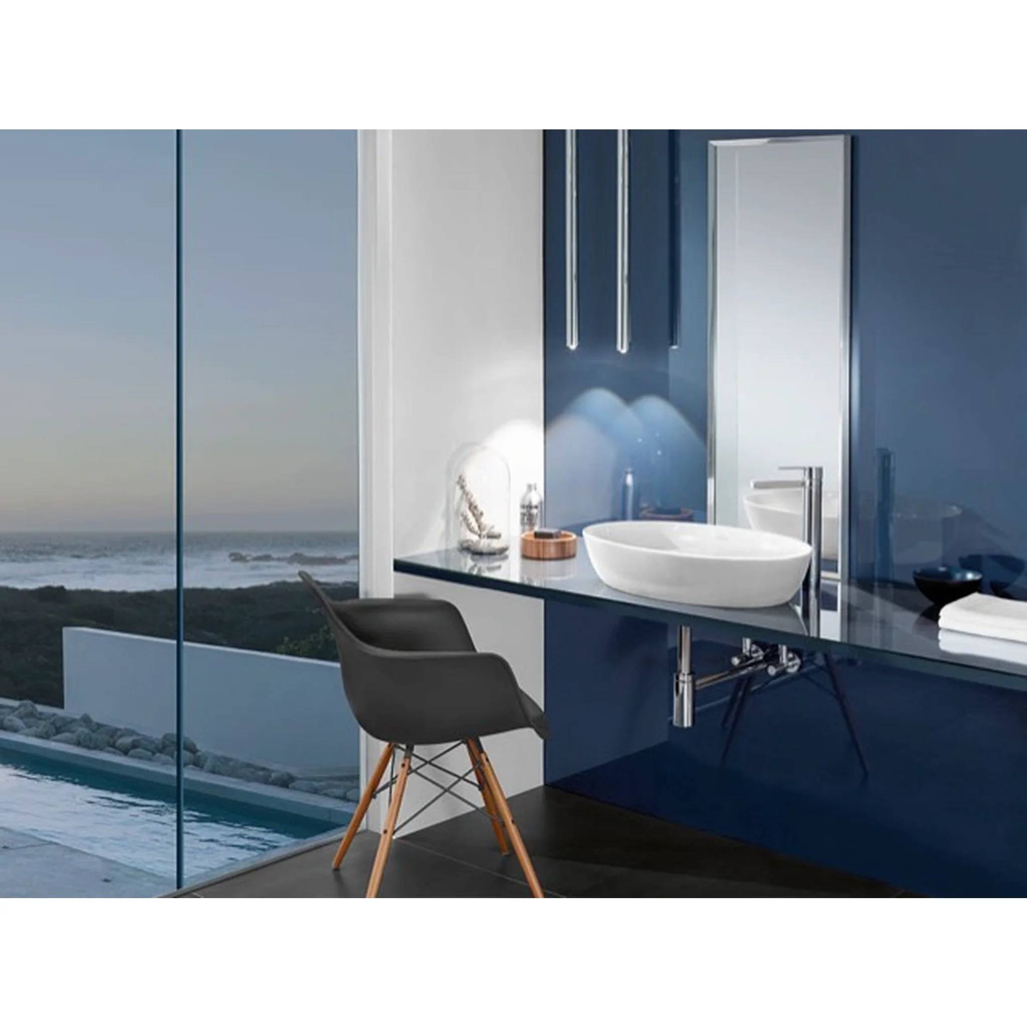 Modernes Badezimmer mit einem Glaswaschtisch und einer Aufsatzschale neben einem Stuhl, mit Blick auf den Ozean durch große Fenster.