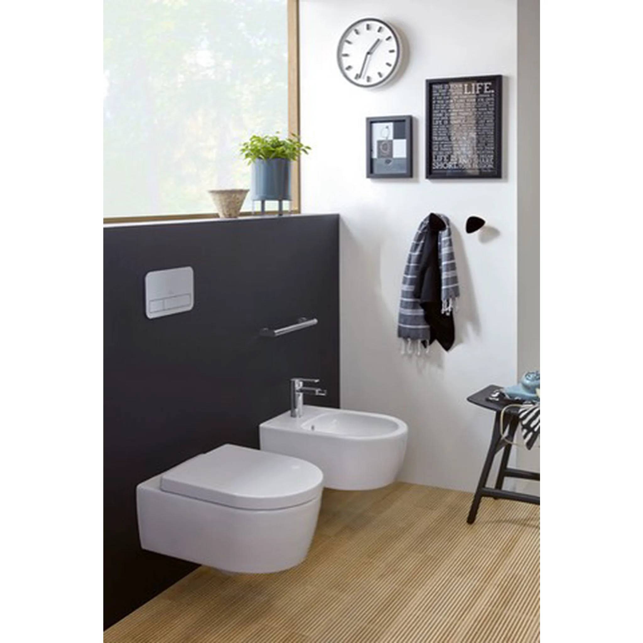 Modernes Badezimmer mit an der Wand montierter Toilette und Bidet, Handtuchhaken, Uhr, Kunstwerk in Rahmen und kleinem Beistelltisch.