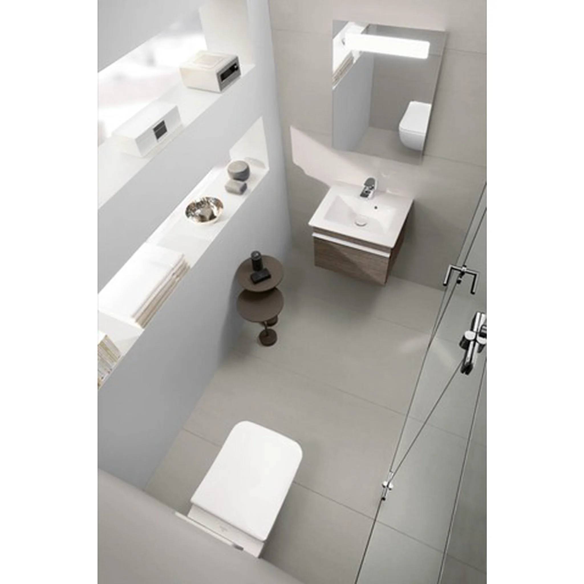 Modernes, minimalistisches Badezimmer mit wandmontiertem Waschbecken und Spiegel, weißen Regalen und einer Toilette, sichtbar in einem kompakten, hell graufliesigen Raum.