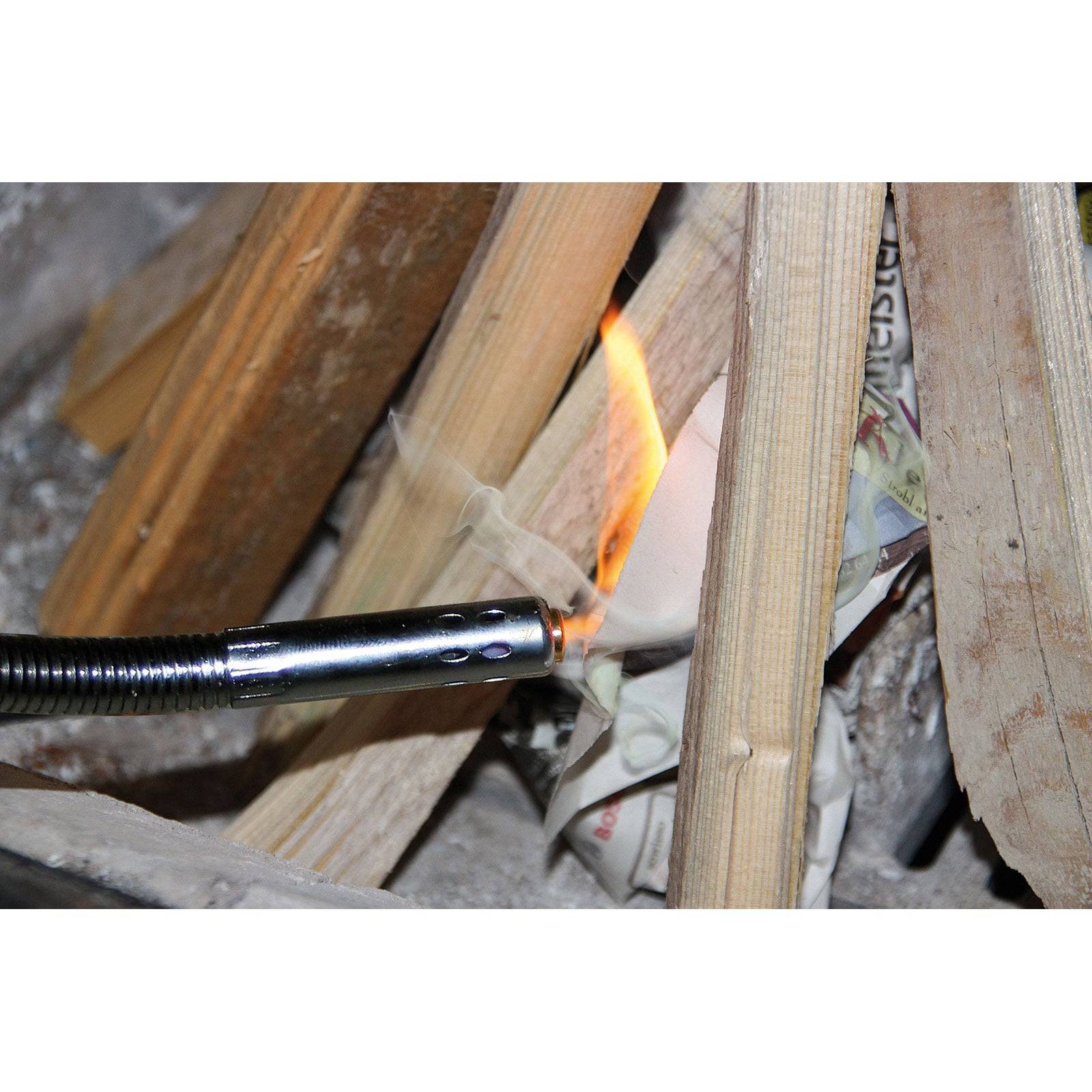 Eine Fackel entzündet ein Stück Zeitungspapier zwischen Holzstäben und demonstriert Techniken zum Feuermachen.