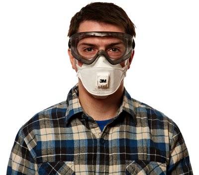 Ein Mann trägt eine Schutzbrille und eine 3M-Atemschutzmaske über einem karierten Hemd vor weißem Hintergrund.