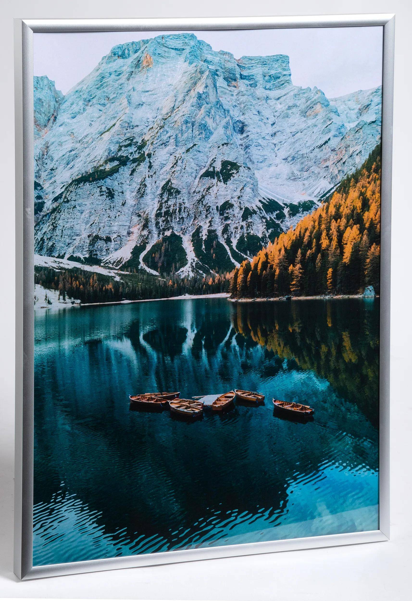 Eine malerische Aussicht auf einen See, umgeben von schneebedeckten Bergen und herbstlichen Kiefern, mit mehreren kleinen Booten, die auf dem ruhigen Wasser treiben.