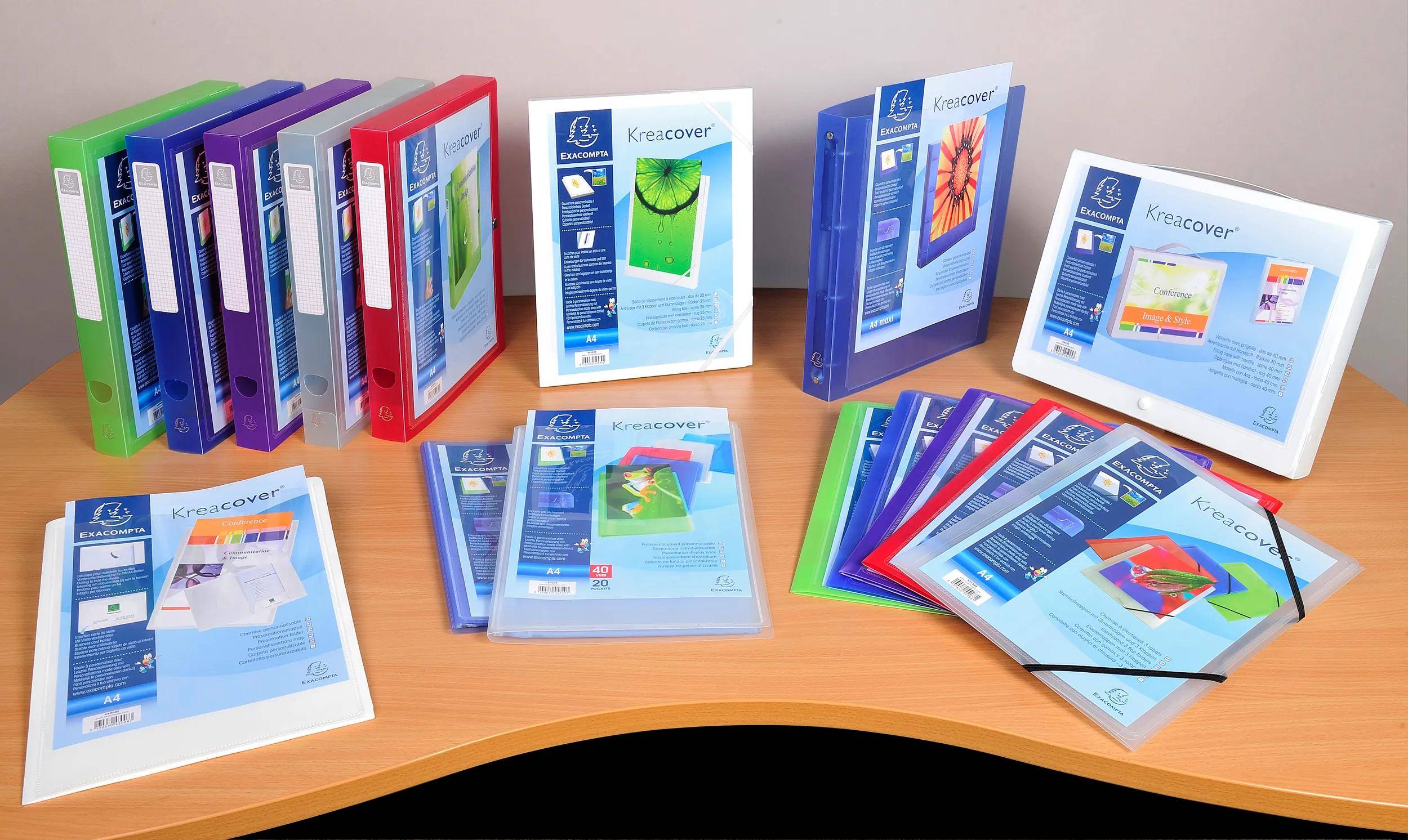 Verschiedenfarbige Dokumentenmappen auf einem Holzschreibtisch, jede mit einem transparenten Umschlag, auf dem unterschiedliche Blumen- und Strukturmuster zu sehen sind.