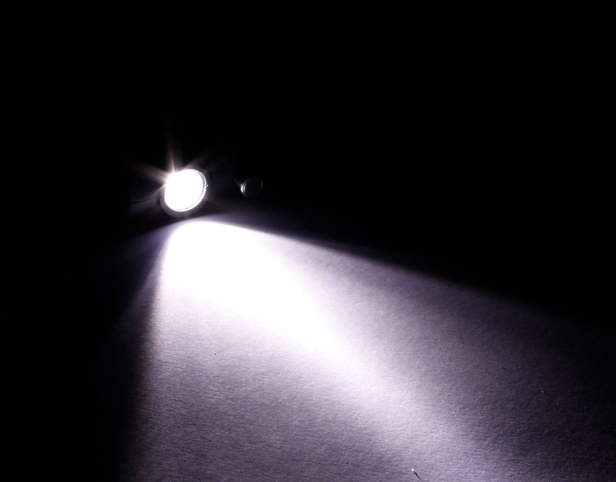 Eine kleine Taschenlampe wirft einen hellen Strahl über eine dunkle Oberfläche, beleuchtet dabei einen Teil der Fläche, während der Rest im Schatten bleibt.