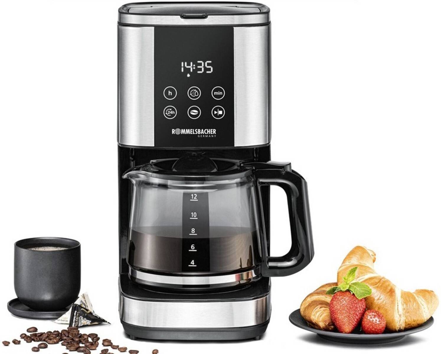 Eine Kaffeemaschine aus Edelstahl mit digitaler Uhr, voller Kaffeekanne, Tasse, Kaffeebohnen, Croissants und Erdbeeren daneben.