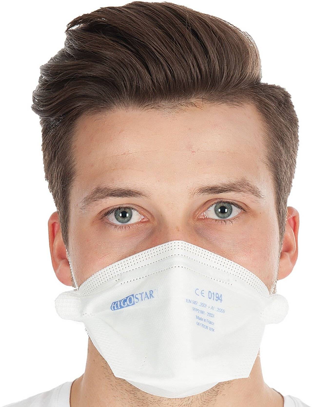 Nahaufnahme eines jungen Mannes, der eine weiße Schutzgesichtsmaske vor einem einfachen weißen Hintergrund trägt.